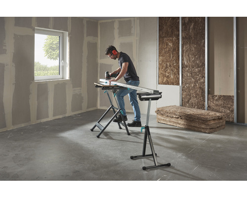 En man arbetar med en sticksåg på ett arbetsstycke på en Wolfcraft arbetsbänk i ett rum med gipsskivor och isoleringsmaterial.