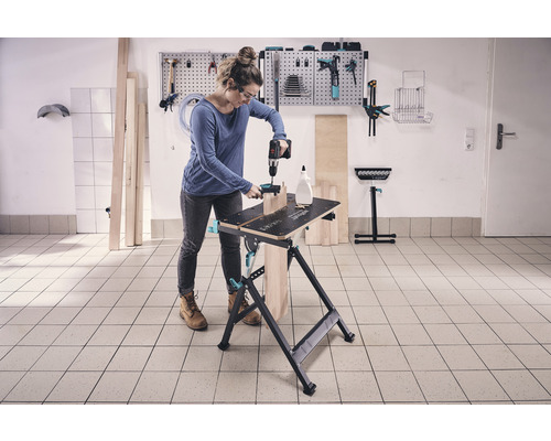 Kvinna arbetar med en borrmaskin på en arbetsbänk i en verkstad.