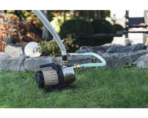 Trädgård med trädgårdspump på gräsmatta för bevattning