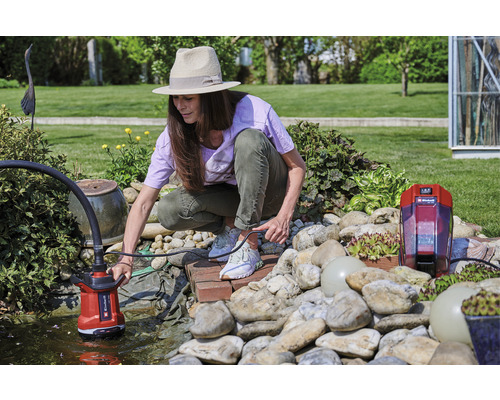 Kvinna använder en dammpump i en trädgårdsdamm.