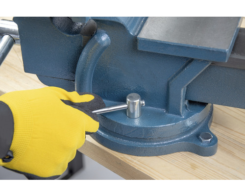 Skruvstäd på arbetsbänk som manövreras av en hand med arbetshandske.