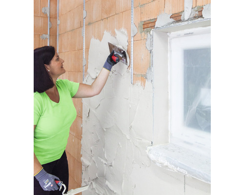 Kvinna applicerar puts på murverk med fönster