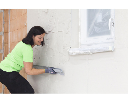 Kvinna jämnar gips med en spackel på en innervägg.