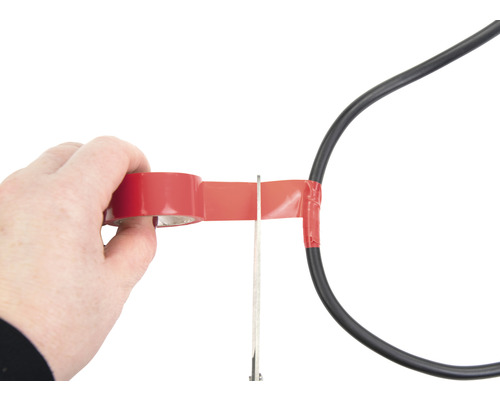 En person isolerar en strömkabel med isoleringstejp och en sax.