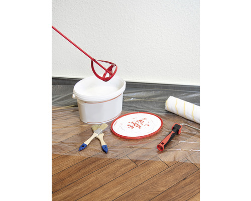 Färgburk, färgblandare, penslar och färgroller på en skyddsfilm för målningsarbeten