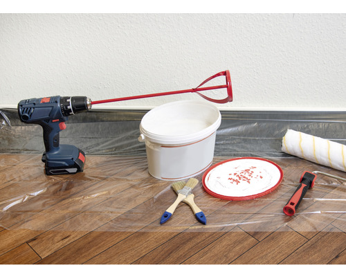 Scen med borrmaskin, färgblandare, färgburk, penslar och färgrulle på en skyddsfilm