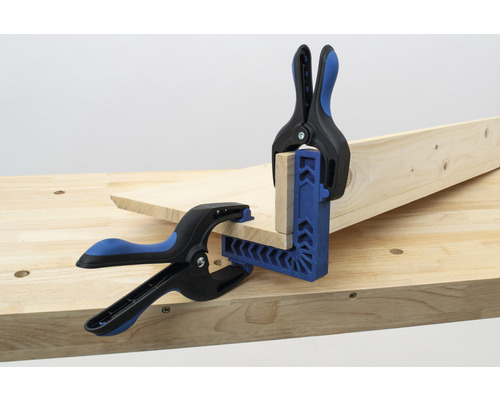 Två träbitar fixeras med en vinkelklämma och fjäderklämmor på en arbetsbänk.