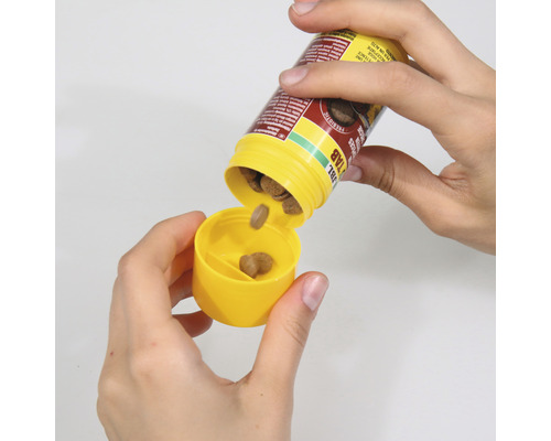 Händer doserar fiskfodertabletter från en gul burk