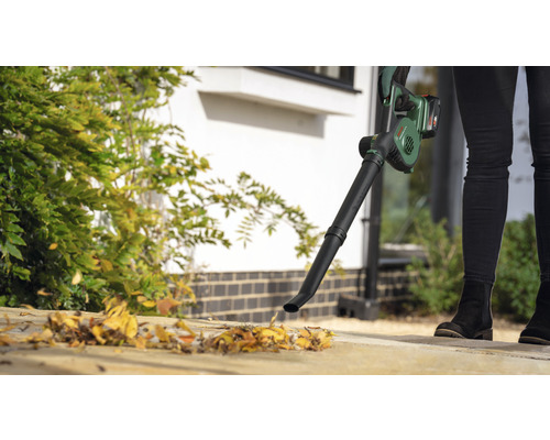 Person använder en sladdlös lövblås för trädgårdsarbete.