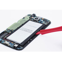 Öppnad smartphone med borttaget batteri och rött verktyg