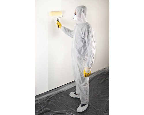 Person i skyddskläder målar en vägg med en roller.