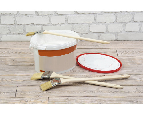 Färghink, penslar och färgtråg framför en tegelvägg