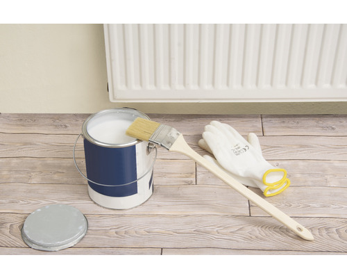 Färghink med färg, pensel och skyddshandskar på trägolv