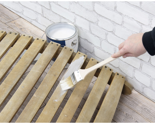 Målning av en träkonstruktion med en pensel bredvid en färgburk