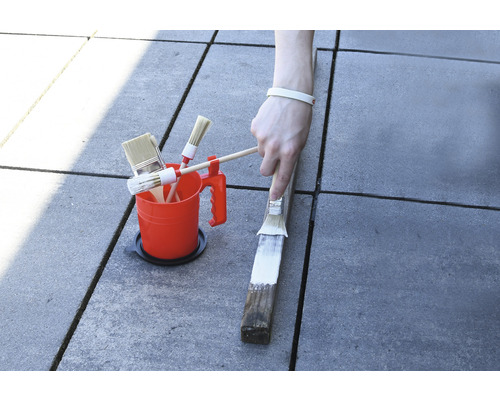 Färghink med olika penslar och målning av en träbit