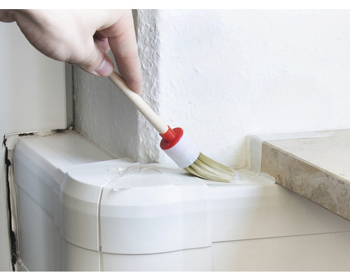 En person målar ett hörn med en rund pensel.