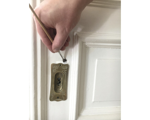 Målning av en vit dörr med en pensel nära ett nyckelhål