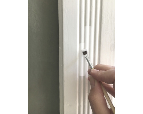 En person målar en vit dekorativ list med en pensel.