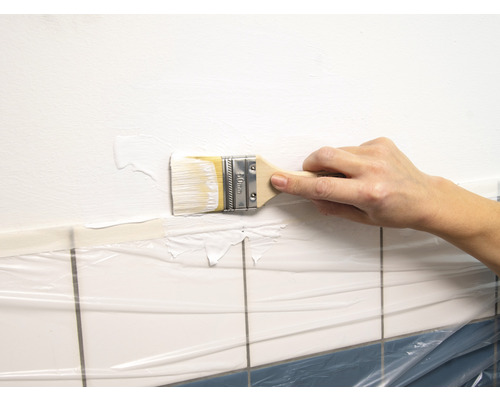 En person målar en vägg ovanför kakel täckt med skyddsfilm med en pensel.