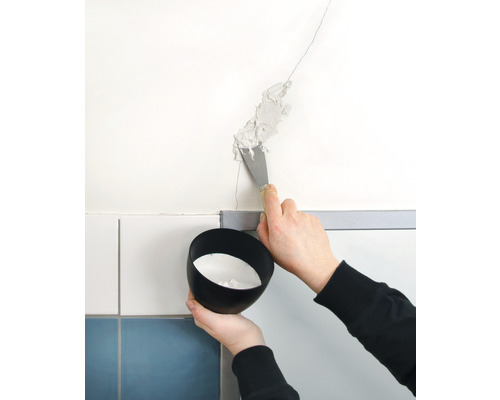 En person fyller en spricka i väggen med en spackel. En skål med fyllnadsmaterial hålls.