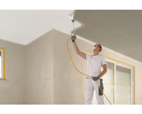 En man använder en färgspruta för att måla ett tak under en rumsrenovering.