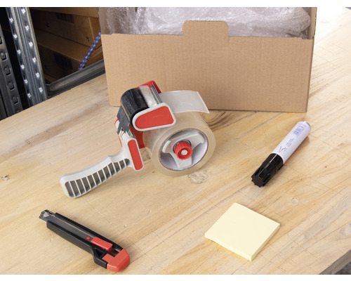 Kartong, tejpdispenser, märkpenna, anteckningsblock och mattkniv på ett bord.
