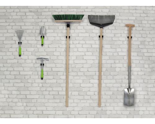 Trädgårdsredskap som kvast, kratta, spade och hacka hänger på en vägg