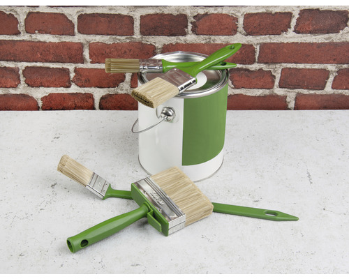 Färghink och olika penslar framför en tegelvägg