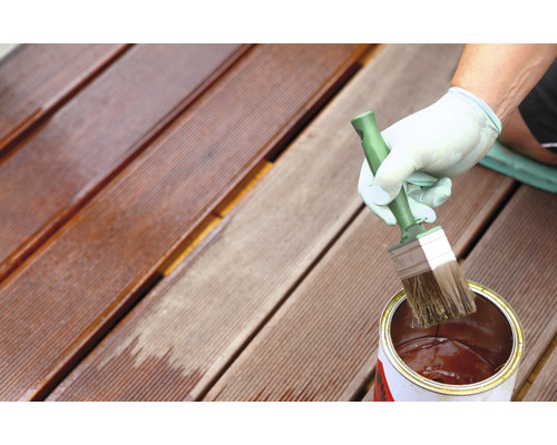 En person oljar en träterrass med en pensel och en burk olja.