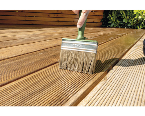 En person målar en träterrass med en platt pensel.