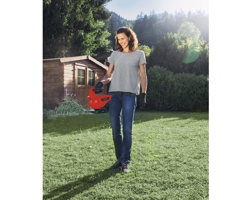 Kvinna använder en elektrisk grässax i trädgården.