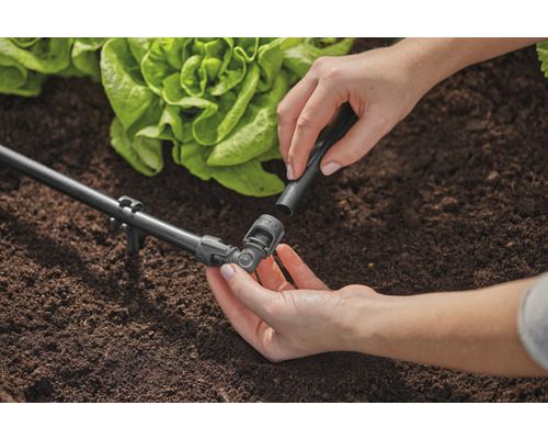 Trädgårdsscen med bevattningssystem och person som fäster en anslutningsdel.