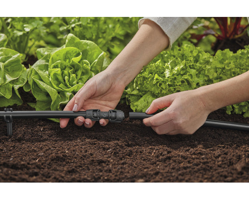 Person kopplar bevattningssystem i trädgårdsrabatt