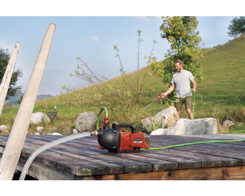 Einhell hydroforpump på en brygga av trä med en man som vattnar med en trädgårdsslang i bakgrunden