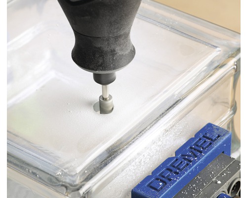 Ett verktyg borrar ett hål i ett glasblock som sitter fast i ett skruvstäd