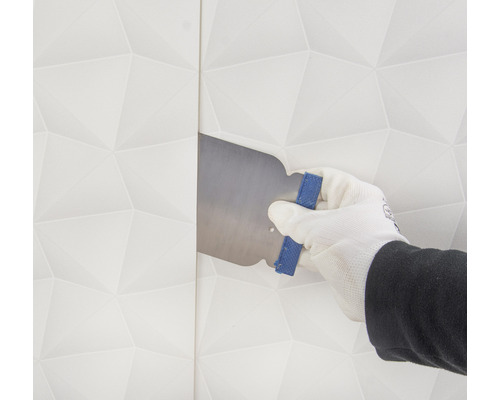 En hand med handske jämnar ut en tapet med en spackel.