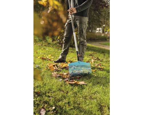 En person krattar löv med en lövräfsa på en gräsmatta.