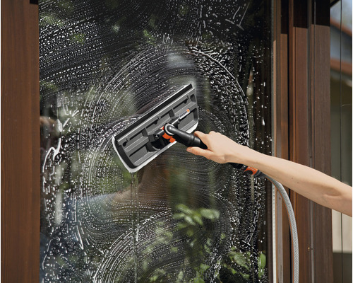 En person rengör ett fönster med en fönsterskrapa och använder tvålvatten.