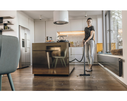 Kvinna dammsuger glassplitter med dammsugare i köket