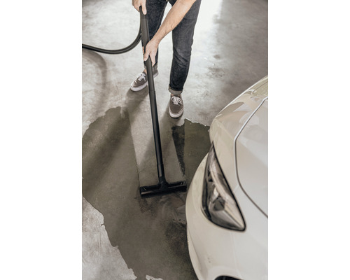 En person rengör en vattenpöl bredvid en bil på ett garagegolv med en våt- och torrdammsugare.