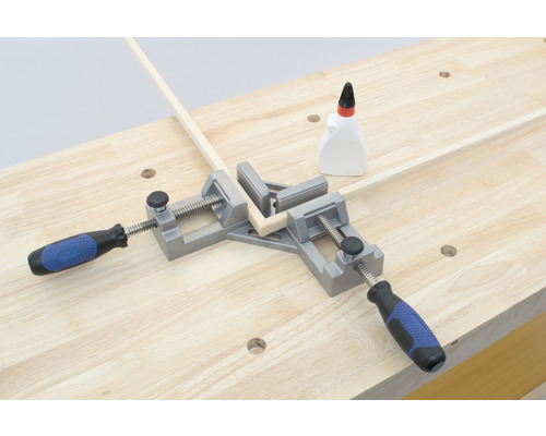 En hörnkäft håller ihop träribbor på en arbetsbänk, tillsammans med en flaska lim.