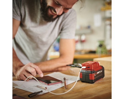 En man laddar sin mobiltelefon med en batteriadapter på en arbetsbänk.