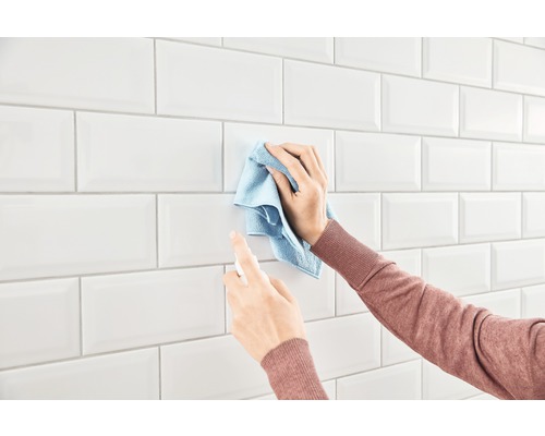 Rengöring av en vägg med vita kakelplattor med en trasa