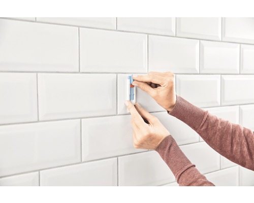 Person fäster ett fästelement för kakel på en kakelvägg
