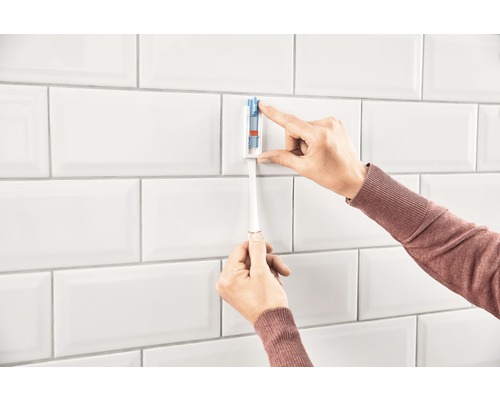 Person fäster ett tandborsthållare på en vit väggplatta.