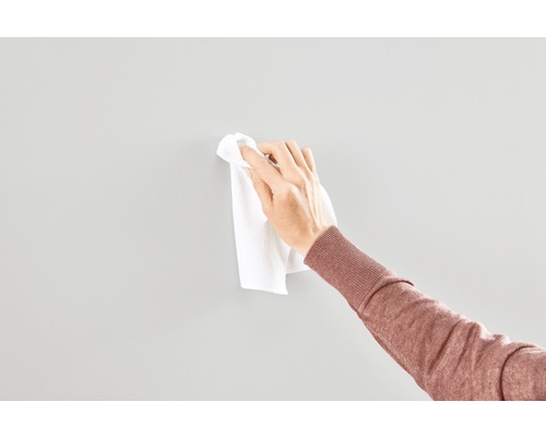 En hand rengör en vägg med en trasa.