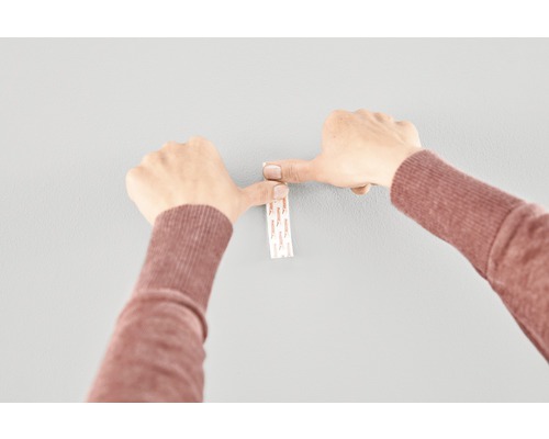 Person som fäster en självhäftande remsa på en vägg