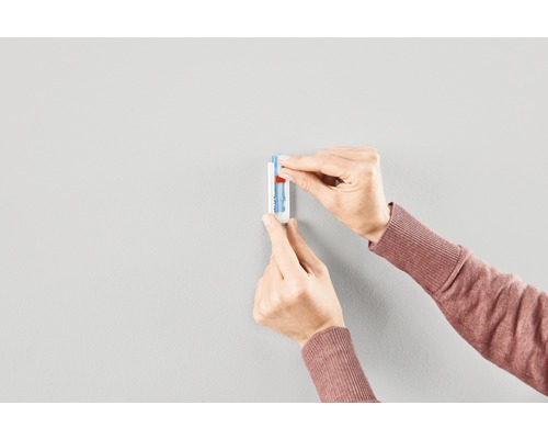 Två händer fäster en bildkrok på väggen.