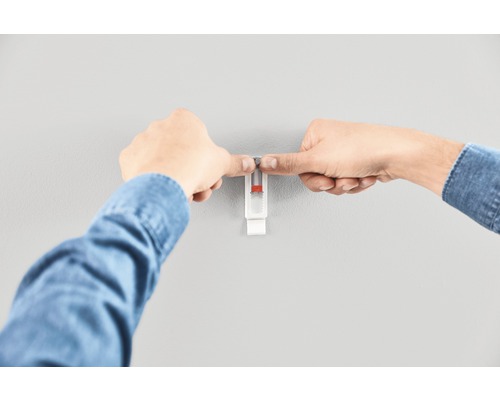 En person fäster en tavelkrok på en vägg.