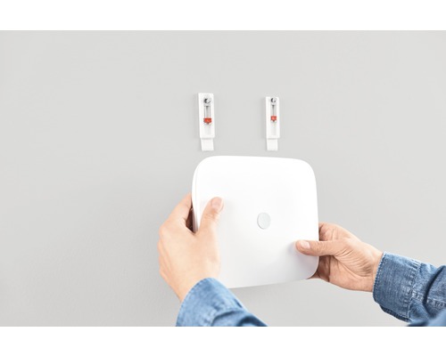 En person monterar en larmsystemcentral på väggen med hjälp av självhäftande krokar.